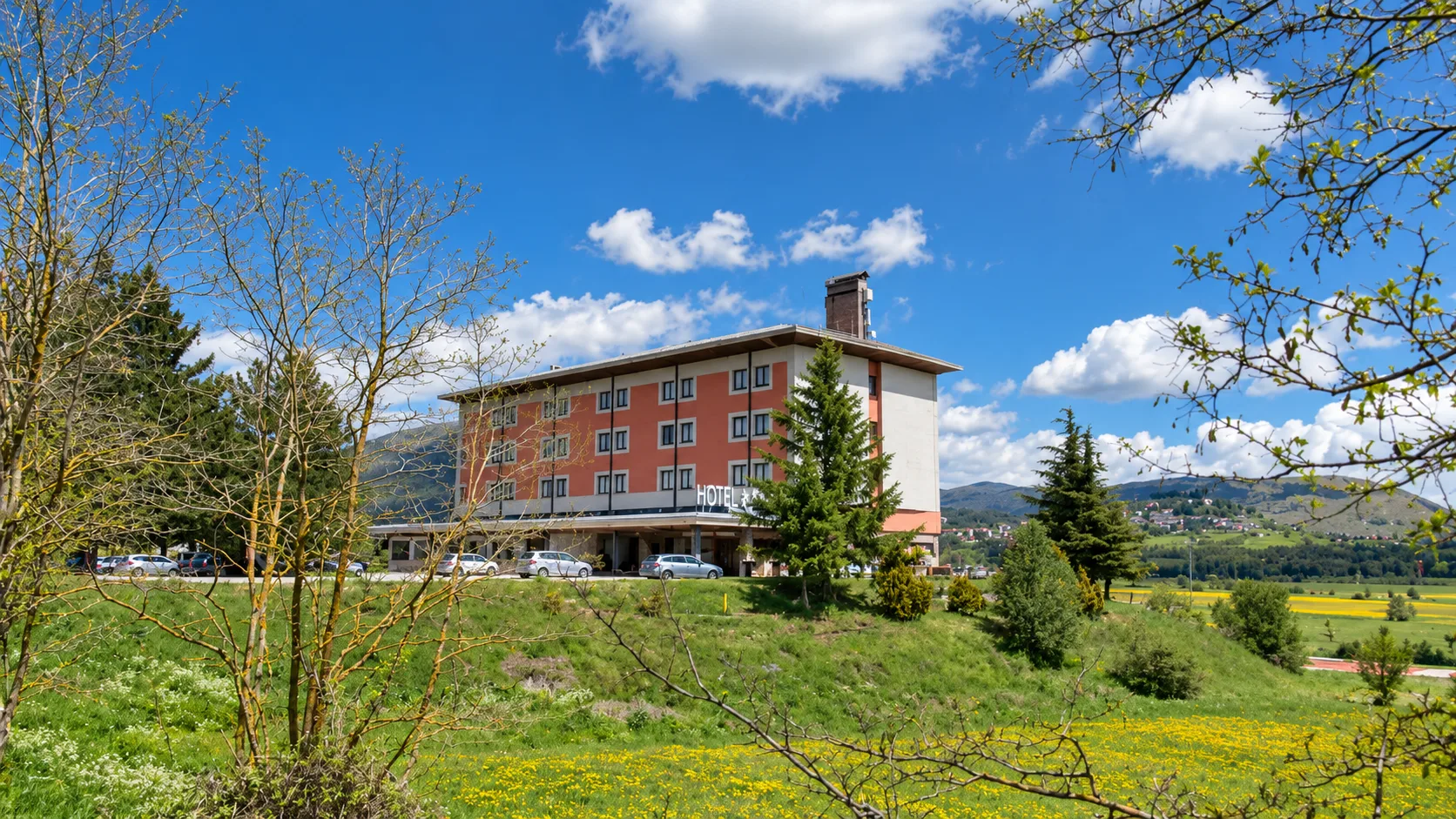 Hotel immerso nel verde con prato fiorito e colline sullo sfondo in primavera