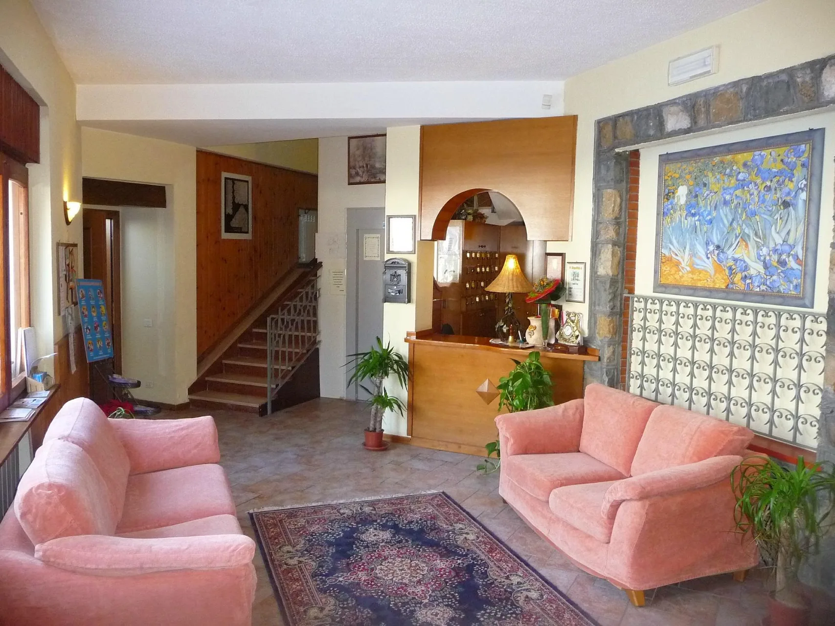 Hall dell'hotel con divani rosa, reception in legno e quadro floreale