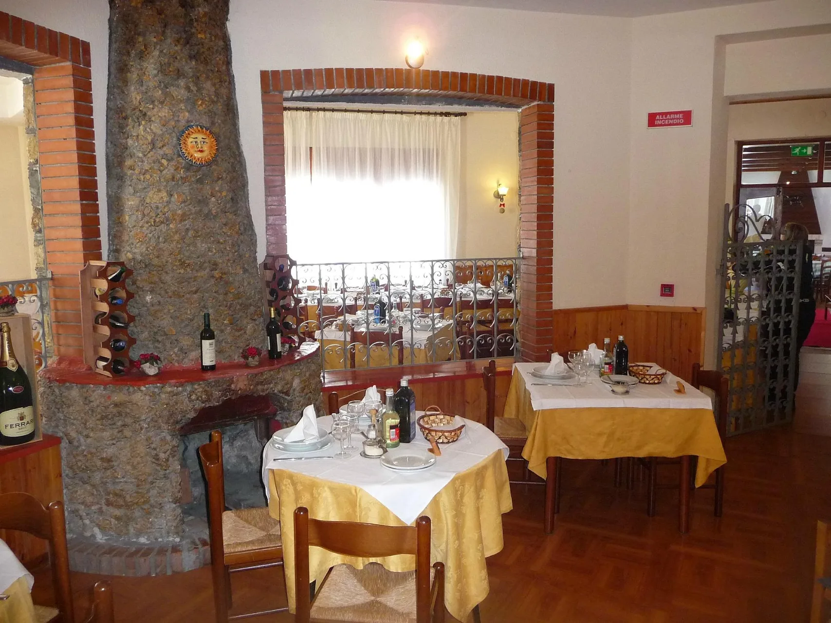 Sala ristorante con tavoli apparecchiati, tovaglie gialle e camino in pietra