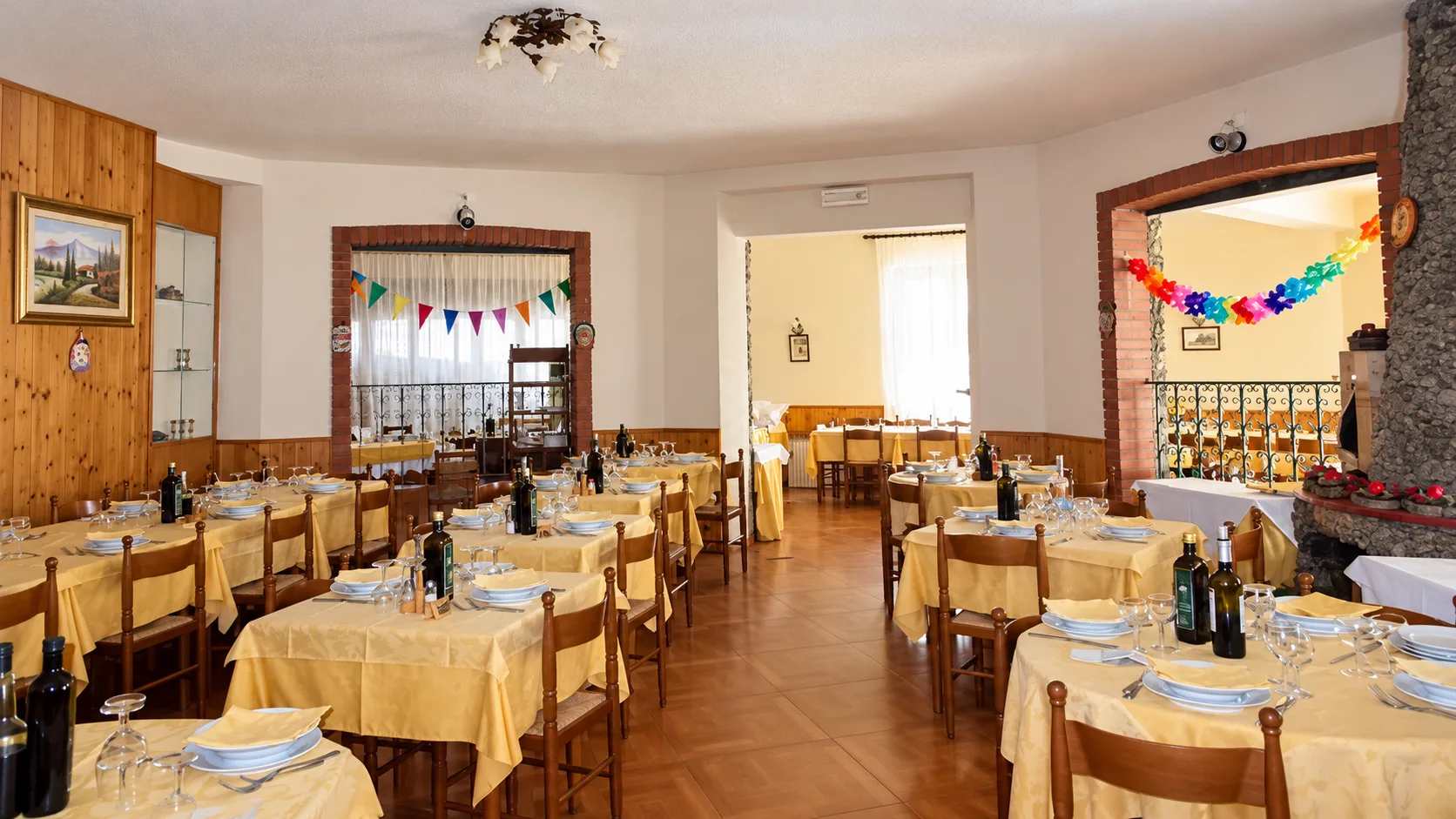 Ampia sala da pranzo con tavoli apparecchiati e decorazioni colorate