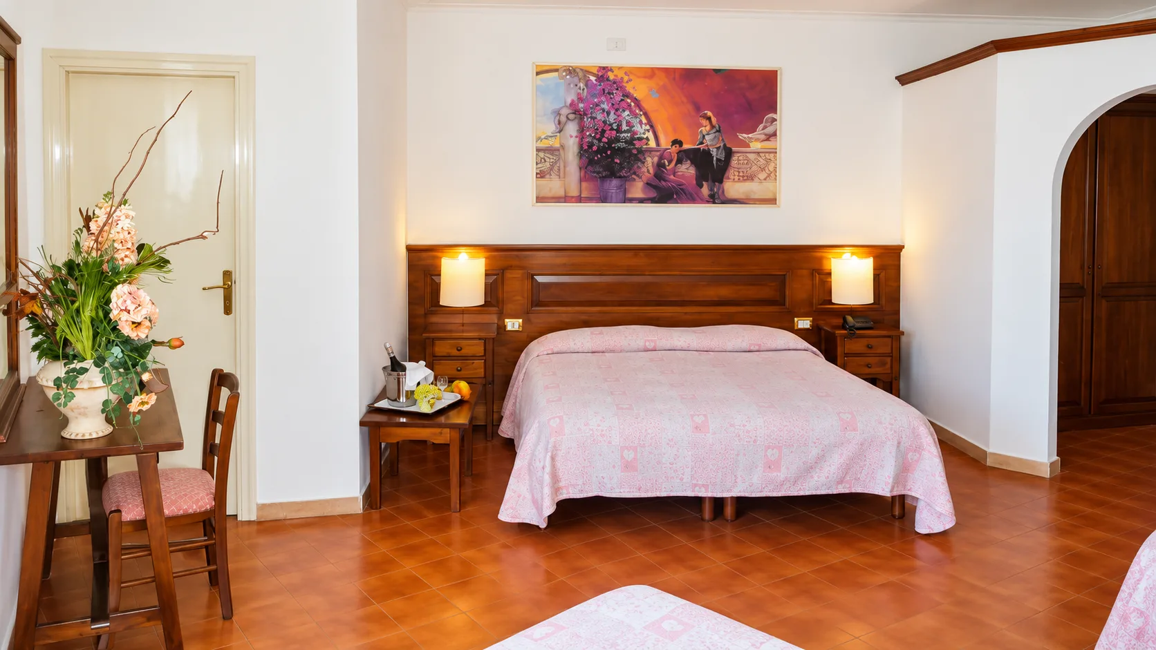 Camera matrimoniale con testiera in legno, copriletto rosa e quadro decorativo